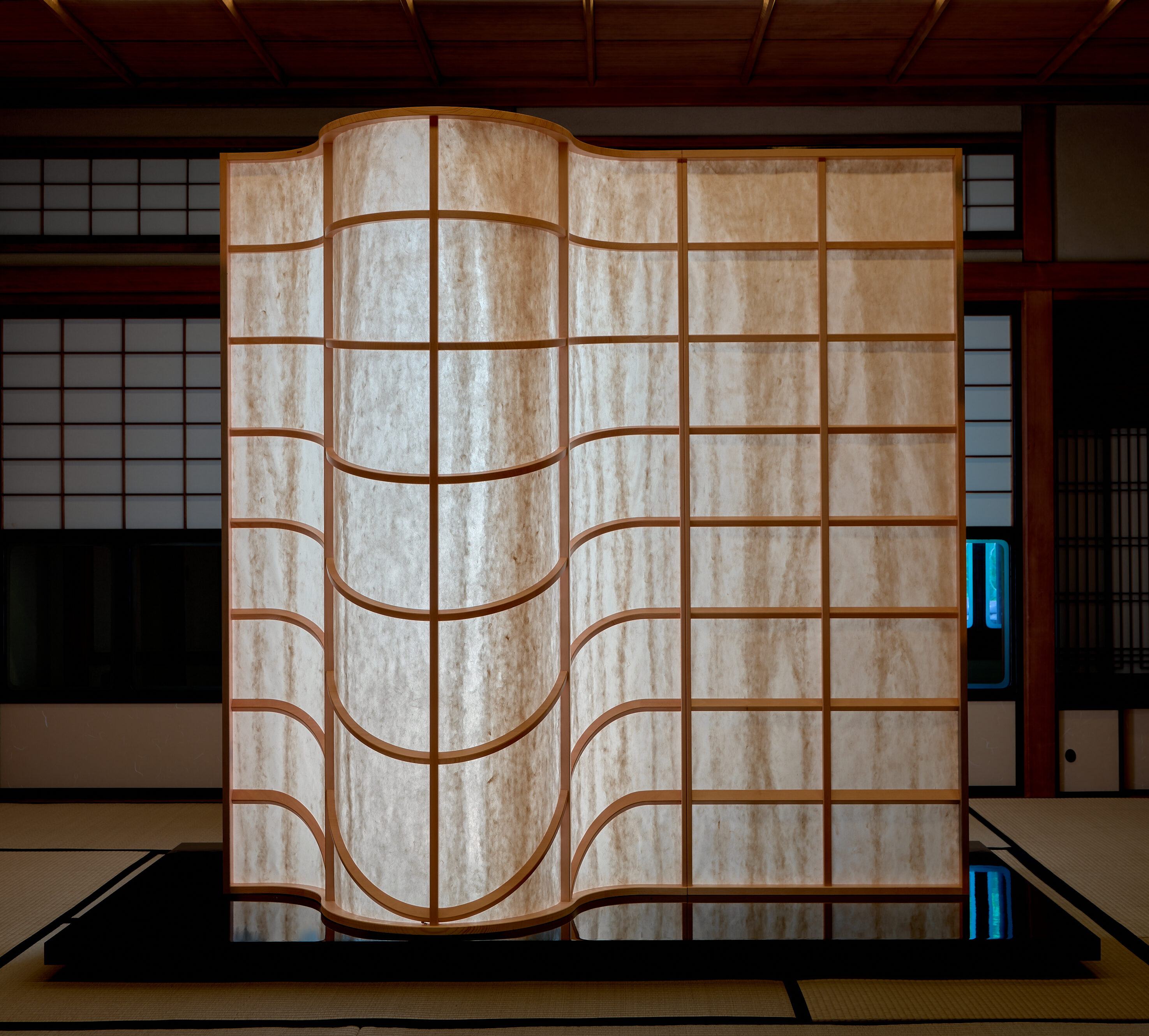 A room divider where the orthogonal grid slowly unweaves itself; rigid wood loosening into curves, Mino Washi paper breathing light